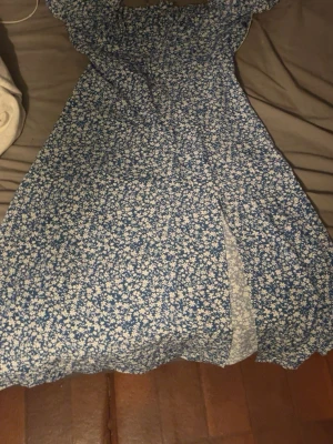 Blå blommig klänning  - Söt blå klänning från SHEIN med vitt blommönster och slits framtill. Klänningen har offshoulder-modell och är gjord i ett lätt material, perfekt för varma dagar. Passar dig som gillar gullig och  somrig stil.