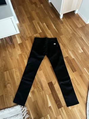 Svarta slim jeans från Replay - Snygga svarta slim fit jeans från Replay med klassisk femficksdesign och diskreta detaljer. Jeansen har raka ben och är tillverkade i ett mjukt, stretchigt material som sitter skönt. Perfekta för dig som gillar en stilren och modern look. De är helt oanvända