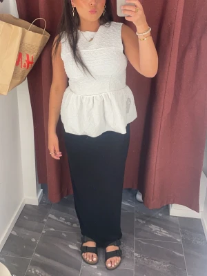 Vit peplumtop med struktur - Snygg vit peplumtop med strukturerat tyg och ärmlös design. Toppen har rund halsringning och markerad midja som ger en feminin siluett. Perfekt att styla med både kjol och jeans. Säljer för att den är för stor, köpt för 599kr säljer för 199kr aldrig använt