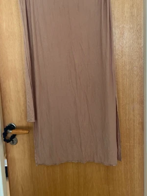 Beige Jersey sjal  - En enkel och stilren beige långklänning i mjukt material. Klänningen har en rak passform och en slits på sidan för extra rörelsefrihet. Perfekt för varma dagar och kan stylas på många olika sätt.