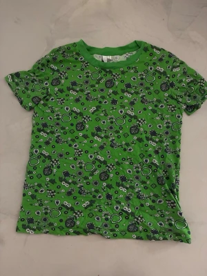 Grön blommig t-shirt - Grön t-shirt med korta ärmar och ett svart vitt blommigt mönster.