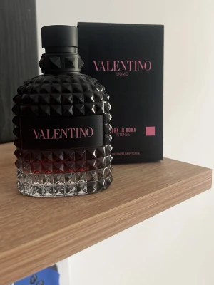 Valentino Uomo Born In Roma Intense EDP 75ml - Lyxig parfym från Valentino, Uomo Born In Roma Intense, i en svart och transparent glasflaska med nitar och rosa detaljer. Flaskan har en unik, edgy design och kommer med originalkartong i svart med rosa text. Perfekt för dig som gillar exklusiva dofter. Doften rymmer 75ml i en 100ml flaska