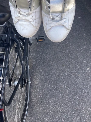 Vita sneakers med silverdetaljer - Säljer ett par vita sneakers med metallic-silver detaljer på sidorna och vid plösen. Klassisk låg modell med vita skosnören och gummisula. Perfekta för dig som vill ha en clean look med lite extra bling.
