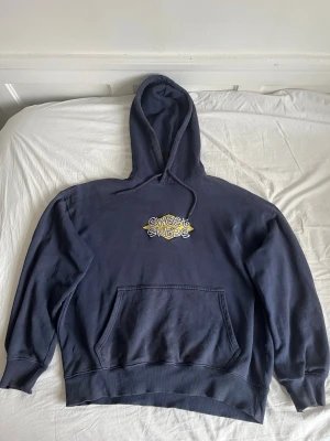 Mörkblå Sweet Skate hoodie - Mörkblå hoodie från Sweet Skate med gul och vit logga på bröstet. Klassisk känguruficka framtill och justerbar huva med snören. Skön och avslappnad passform, perfekt till streetwear-stilen. Tillverkad i mjukt bomullsmaterial.