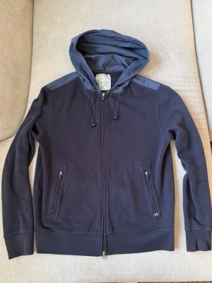Boggi Milano Hoodie / Ziptröja –  strl M – Mörkblå - Säljer en stilren hoodie från Boggi Milano i mörkblå färg. Modellen har huva, tvåvägsdragkedja framtill och dragkedjeförsedda fickor. Tillverkad i ett kraftigare och kvalitativt material som passar både till vardags och för en mer uppklädd casual stil.  Storlek: M Färg: Mörkblå / Navy Skick: Fint begagnat skick  • Boggi Milano • Tvåvägsdragkedja • Dragkedjefickor • Justerbar huva • Mjuk och bekväm passform • Stilren design