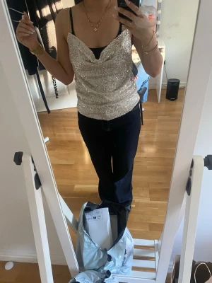 Glittrig silver linnetopp med paljetter - Snygg glittrig linnetopp i silver med tunna axelband och draperad framsida. Toppen är täckt av paljetter och har en croppad passform som ger en trendig look. Perfekt för dig som vill sticka ut och glänsa.