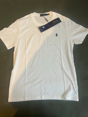 Vit t-shirt från Polo Ralph Lauren - Klassisk vit t-shirt från Polo Ralph Lauren med rund halsringning och den ikoniska broderade loggan på bröstet. Tillverkad i mjuk bomull för en skön känsla och perfekt passform. Enkel och stilren design som funkar till allt.