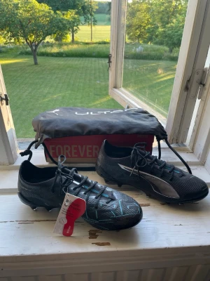 Fotbollskor Puma - HELT NYA Puma ultra elit fotbollskor från Unisport (2500)! Dobbar på  tillverkad för AG.   ⚫️Glittrig svart blå färg med silverdetaljer 🔵                 📏Storlek 40 📏📦Box ingår 📦 🎒Påse ingår🎒