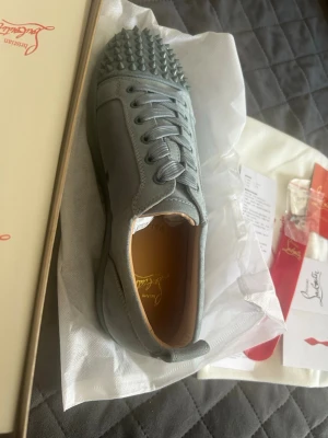 Blå Louboutin sneakers med nitar - Snygga blå sneakers från Christian Louboutin i läder med ikoniska nitar på tån. Skorna har rundad tå, matchande blå skosnören och klassisk röd innersula med logga. Perfekta för dig som vill sticka ut med en edgy och exklusiv stil. Kan mötas i Västerås 