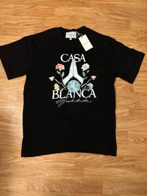 Svart t-shirt från Casablanca - Snygg svart t-shirt från Casablanca med tryck framtill som visar blommor och texten 'Casa Blanca'. Klassisk passform och rund hals. Tillverkad i mjuk bomull som känns skön mot huden. Perfekt för dig som gillar stilrena plagg med coola detaljer.