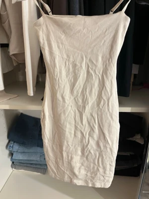 Beige kort klänning från Zara - Säljer en enkel och stilren beige kort klänning från Zara. Klänningen har smala axelband och en rak passform som ger en clean look. Perfekt för varma dagar eller att styla med en kavaj. Materialet känns mjukt och lätt mot huden.
