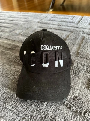 Svart Dsquared2 ICON keps - Säljer en svart keps från Dsquared2 med stor, vit och svart 3D-broderad text 'ICON' framtill. Klassisk böjd skärm och justerbar rem bak. Tillverkad i bomullstyg som ger en skön och avslappnad look. Perfekt för dig som vill sticka ut med en trendig accessoar.