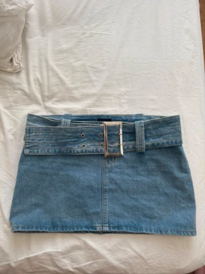 Blå jeanskjol med bälte - Trendig blå jeanskjol med bredt bälte och stor silverfärgad spänne❣️Såå snygg passform och passar till allt. Kjolen är kort och har en klassisk denimlook med synliga sömmar. Priset kan diskuteras vid snabb affär