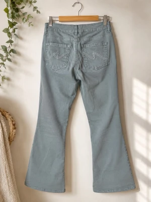 Gröna bootcut jeans med fickdetaljer - Snygga gröna bootcut jeans med klassiska fem fickor och dekorativa sömmar på bakfickorna. Jeansen har hög midja och utsvängda ben för en retroinspirerad look. Perfekta för dig som vill ha en avslappnad men trendig stil.