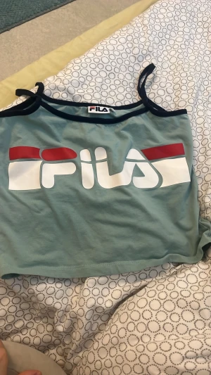 Turkos linnetopp från FILA - Snygg turkos linnetopp från FILA med mörkblå axelband och stort logotryck framtill.