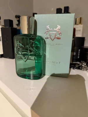 Parfums de Marly Greenley EdP - Greenley från Parfums de Marly är en exklusiv parfym i en stilren, grön glasflaska med silverfärgat lock. Flaskan har en elegant relief med två hästar och sköld, och doften är fräsch och modern. Perfekt för dig som gillar lyxiga och unika parfymer. Ungefär 60 ml kvar av 120 ml