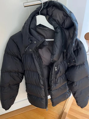 Svart dunjacka från Ralph Lauren - Säljer en svart dunjacka från Ralph Lauren med avtagbar luva. Storleken är troligen medium, även om lappen inte är kvar. Väl omhändertagen och i bra skick.