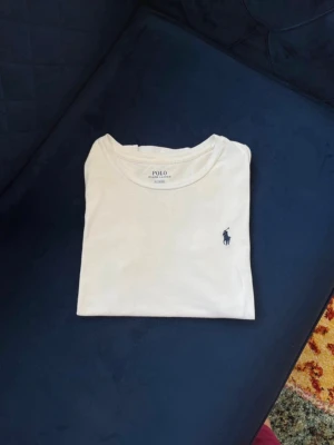 Äkta polo Ralph Lauren T-shirt, vit - Klassisk vit t-shirt från Polo Ralph Lauren med den ikoniska mörkblå broderade loggan på bröstet. T-shirten har rund halsringning och är tillverkad i mjuk bomull för en skön känsla. Perfekt basplagg till garderoben. NYPRIS: 1095kr. OBS: Accepterar alla bud!