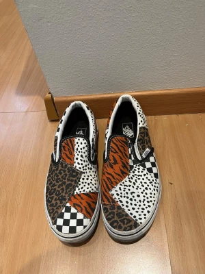 Vans slip-on sneakers djurmönster - Unika Vans slip-on sneakers med patchwork-design i flera mönster: leopard, tiger, dalmatin och klassiskt svartvitt schackrutigt. Färgerna är svart, vitt, orange och brunt. Skorna har låg profil och elastiska sidor för enkel påtagning. Perfekta för dig som vill sticka ut.