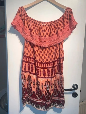 Mönstrad offshoulder klänning Hollister - Säljer en kort offshoulder klänning från Hollister i ljusrosa och vinröda toner. Klänningen har ett bohemiskt mönster, bred volang upptill och är ärmlös. Perfekt för sommardagar och festivaler. Tillverkad i mjuk bomull för skön känsla.