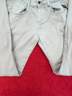 Benvita  jeans från Replay - Säljer ett par benvita jeans från Replay  med klassisk femficksdesign och raka ben. Jeansen har detaljerade sömmar på bakfickorna och bälteshällor. Materialet är mjukt och bekvämt, perfekt för en avslappnad stil. W34