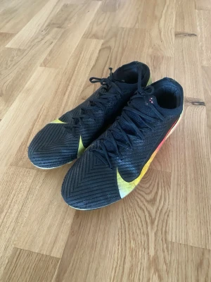 Nike Mercurial svarta fotbollsskor - Säljer ett par Nike Mercurial fotbollsskor i svart, med gula, grön och röda detaljer. Skorna är använda en få tal gånger och sitter riktigt fint. Det är bara att höra av sig för intresse. 