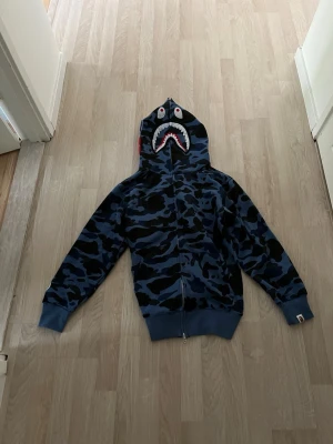 Bape - Snygg blå hoodie från bape i mjukt bomullsmaterial. Klassisk modell med huva och ribbade muddar. Perfekt för dig som gillar streetwear och vill ha en enkel men stilren look.