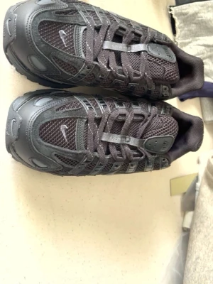 Black Nike P6000 - Säljer ett par svarta Nike sneakers med cool design. Skorna har en mix av mesh och läderdetaljer, samt tydliga swoosh-loggor på sidan. Snygga snörningar och robust sula ger en sportig vibe. Perfekta för dig som gillar streetwear och vill ha något stilrent.