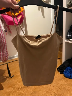 Beige linnetopp med tunna band - Säljer en enkel och stilren beige linnetopp med tunna axelband. Toppen har en lätt draperad ringning och är perfekt för varma dagar. Passar till både jeans och kjol för en avslappnad look.