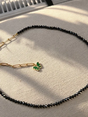 Svart pärlhalsband med fjäril och hjärta - Unikt halsband med gröna sandstenar, guldfärgade länkar och en grön fjärilsberlock. Halsbandet har även ett hängande vitt hjärta i pärlemor. Perfekt för dig som gillar trendiga detaljer och mixade material.