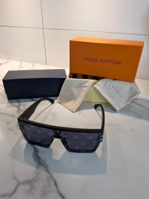 Louis Vuitton svarta monogram solglasögon - Säljer ett par svarta Louis Vuitton solglasögon med bred, rektangulär form och ikoniskt monogrammönster på glasen. Snygg och modern design med robust båge. Kommer med originalbox och putsduk.