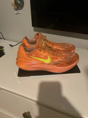Nike Gt cuts 2  - Säljer ett par riktigt snygga orange sneakers från Nike med en iögonfallande gul swoosh på sidan. Skorna har en låg profil och coolt mönstrad ovandel i textil och syntet. Perfekta för dig som vill sticka ut med färg och stil.