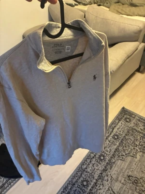 Beige halfzip från Polo Ralph Lauren - Snygg beige långärmad halfzip-tröja från Polo Ralph Lauren med klassisk broderad logga på bröstet. Tröjan har hög krage med dragkedja och är tillverkad i mjukt bomullsmaterial. Perfekt för en avslappnad och stilren look.