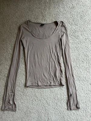 Beige långärmad topp Gina Tricot - Säljer en enkel och stilren beige långärmad topp från Gina Tricot. Toppen har en rundad, djup urringning och är figurnära i modellen. Perfekt att matcha med jeans eller kjol för en clean look.