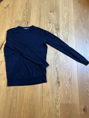 Mörkblå tröja från Dressmann - En stilren mörkblå långärmad tröja från Dressmann i klassisk modell. Tröjan har rund halsringning och är tillverkad i bomull, vilket gör den både mjuk och bekväm. Perfekt för en enkel och clean look.