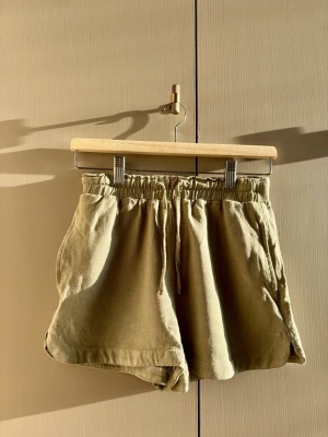 Gröna shorts med snörning - Snygga gröna shorts med elastisk midja och snörning framtill. De har en loose passform och är tillverkade i ett mjukt linnematerial, perfekta för varma dagar. Shortsen har fickor i sidorna och en avslappnad vibe.