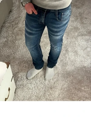 Blå jeans från replay med slitningar - Snygga blå jeans från replay med diskreta slitningar och tvättade detaljer på låren och knäna. Klassisk femficksmodell med dragkedjegylf och smal passform. Perfekta för en trendig och avslappnad look.