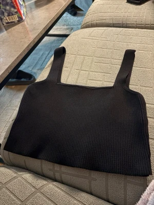 Svart ribbad crop top - En svart ribbad crop top med breda axelband och fyrkantig halsringning. Toppen är enkel och stilren, perfekt att matcha med jeans eller kjol. Materialet är stretchigt och bekvämt. Pasar nog xs oxå