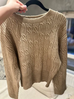 Beige kabelstickad tröja - beige kabelstickad tröja med rund halsringning och långa ärmar. Tröjan har ett klassiskt kabelmönster och ribbade muddar vid ärmslut och nederkant. Den är från Lindex och är i storlek S. Har bara kommit till användning en gång så är som ny.