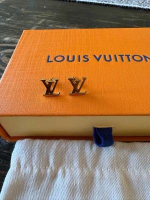 Louis Vuitton guldiga örhängen - Snygga örhängen i guldton från Louis Vuitton med den ikoniska LV-loggan. De är små, stilrena och perfekta för dig som gillar exklusiva accessoarer. Kommer med original ask och dustbag från Louis Vuitton.