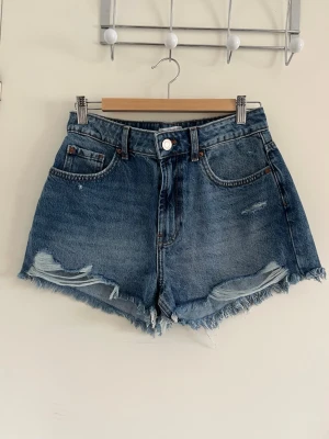 Blå shorts😇😇 - Säljer ett par blå denimshorts från Primark som är min wast med ”trasiga kanter”. Shortsen har slitna detaljer framtill och klassiska fickor, som ger shortsen en snygg stil. Perfekta för sommaren!! Skulle tipsa om att stila dem med en vit lose tröja och smycken!!✌🏼😊.                         ⚠️har aldrig använt dem, men lappen finns inte kvar