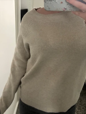Beige stickad tröja med rund hals - En stilren beige stickad tröja med rund halsringning och långa ärmar. Tröjan har ribbstickade muddar vid ärmslut och nederkant. Perfekt för lager-på-lager och enkel att matcha med olika outfits.