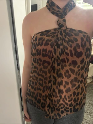Leopardmönstrad halterneck topp - Snygg leopardmönstrad halterneck topp i tunn, luftig polyester. Toppen är ärmlös och knyts i nacken för en trendig look. Perfekt för dig som vill sticka ut med ett djurmönster och en cool siluett . Säljer då den tyvärr inte kommit till användning så helt oanvänd endast testad
