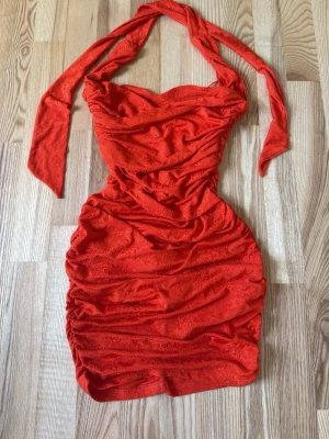 Röd omlottklänning med snörning - Aldrig använt Snygg röd kortklänning med omlott och snörning i halsen. Klänningen har åtsittande passform, draperade detaljer och är ärmlös. Perfekt för dig som vill sticka ut med en färgstark look.