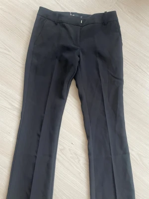 Bootcut kostymbyxor från BikBok - Snygga svarta kostymbyxor med klassisk passform och raka ben. Byxorna har hällor för skärp och diskreta sidofickor. Perfekta för en stilren look och passar till många olika outfits.