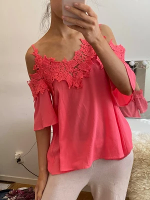 Rosa offshoulder topp med spetsdetaljer - Superfin rosa offshoulder topp med breda spetsdetaljer över axlarna och lös passform. Toppen har korta ärmar och är perfekt för dig som vill sticka ut med en färgglad och feminin look.