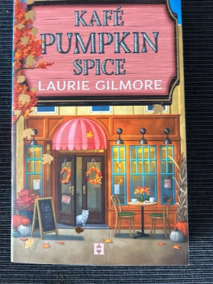 Kafé Pumpkin Spice av Laurie Gilmore - En färgglad pocketbok med titeln 'Kafé Pumpkin Spice' av Laurie Gilmore. Omslaget har höstmotiv med orange och rosa toner, caféillustration och löv. Boken är feelgood och utspelar sig i en mysig småstad, med inslag av romantik och höststämning.