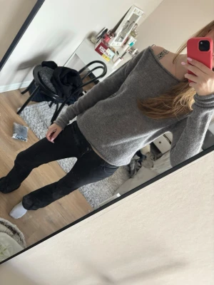 Grå off shoulder stickad tröja - Mysig grå stickad tröja med off shoulder-design och långa ärmar. Tröjan har en enkel, rak passform och är perfekt för lager-på-lager. Materialet ser ut att vara mjukt och bekvämt, vilket gör den skön att bära under kyliga dagar.