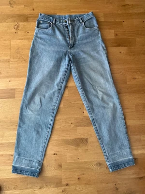 Ljusblå high waist mom jeans - Säljer ett par ljusblå mom jeans med hög midja och raka ben. Klassisk femficksmodell med dragkedja och knapp framtill. Jeansen har en avslappnad passform och är tillverkade i bomullsdenim.