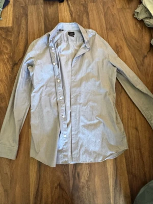 Ljusblå skjorta från Selected Homme - Klassisk ljusblå skjorta från Selected Homme med regular fit. Skjortan har diskret rutigt mönster, långa ärmar och knappar framtill. Tillverkad i bomull och enkel att stryka. Perfekt för en clean och stilren look.